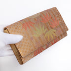 Bronze-gold Japanese silk envelope clutch with bamboo and floral design, held in a white-gloved hand at a three-quarter angle