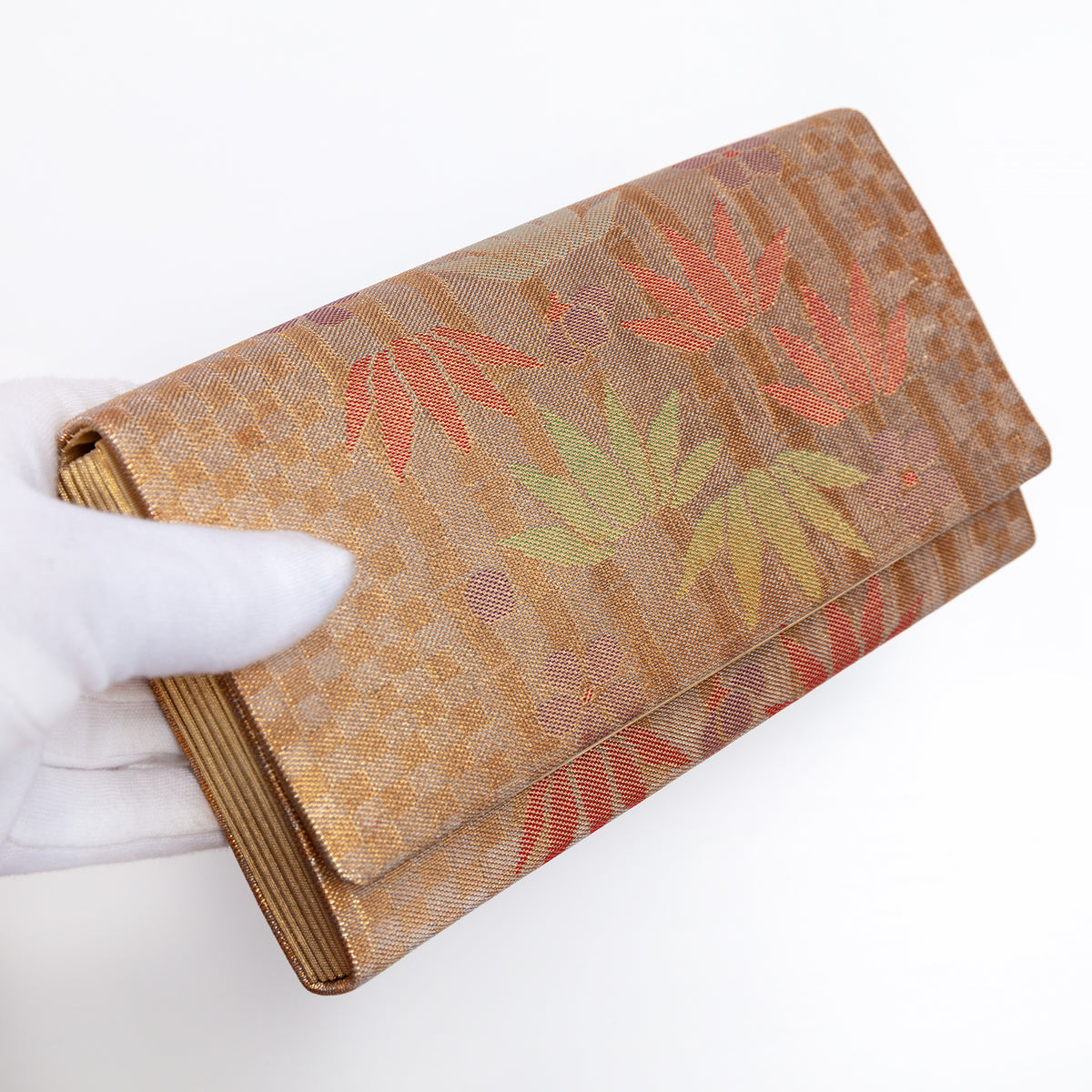 Bronze-gold Japanese silk envelope clutch with bamboo and floral design, held in a white-gloved hand at a three-quarter angle