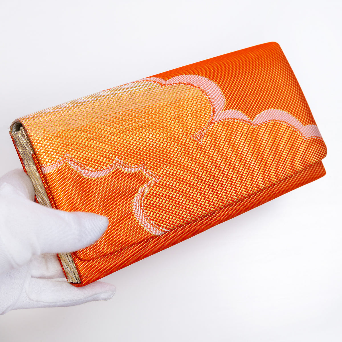 Metallic orange Japanese silk foldover clutch with gold cloud design, held in a white-gloved hand at a three-quarter angle
