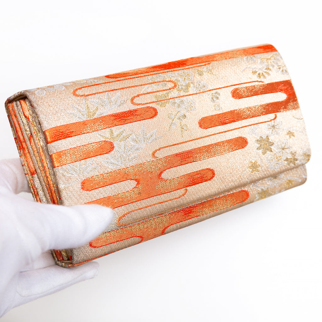 Pale gold Japanese silk envelope clutch with kasumi mist design, held in a white-gloved hand at a three-quarter angle
