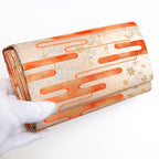 Pale gold Japanese silk envelope clutch with kasumi mist design, held in a white-gloved hand at a three-quarter angle