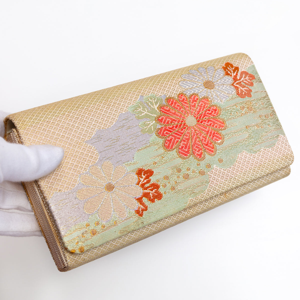 Gold Japanese silk foldover clutch with pale mint green accent and chrysanthemum motif, held in a white-gloved hand at a three-quarter angle
