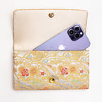Open silver and gold Japanese silk envelope clutch shown with iPhone 14 Pro Max for scale