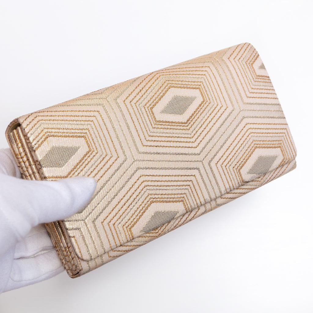 Pale gold Japanese silk foldover clutch with geometric hexagon design, held in a white-gloved hand at a three-quarter angle