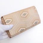 Pale gold Japanese silk foldover clutch with geometric hexagon design, held in a white-gloved hand at a three-quarter angle