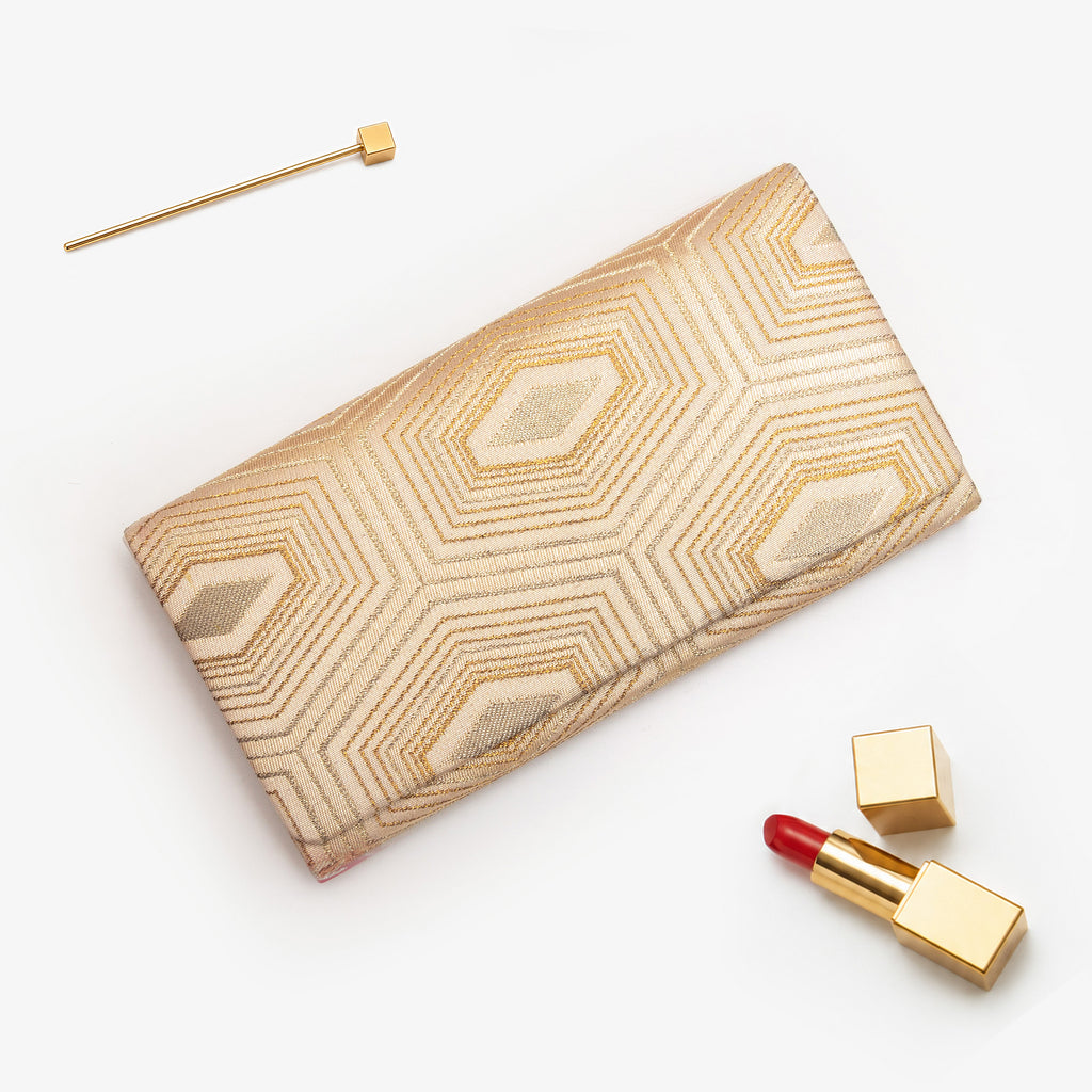 Pale gold Japanese silk foldover clutch with bold nested hexagon design, shown in styled flatlay