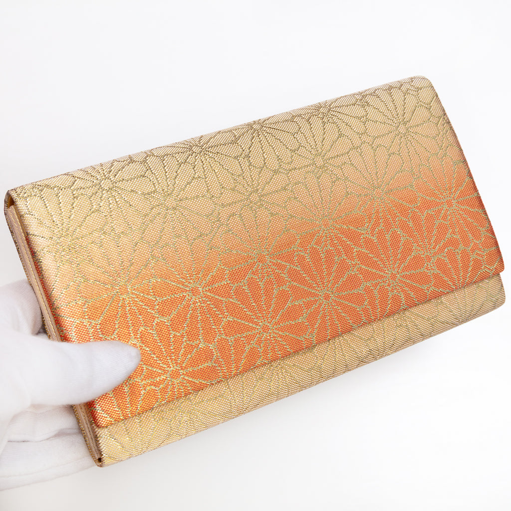 Gold and orange Japanese silk foldover clutch with chrysanthemum ombré design, held in a white-gloved hand at a three-quarter angle