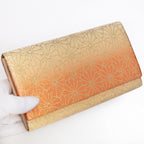 Gold and orange Japanese silk foldover clutch with chrysanthemum ombré design, held in a white-gloved hand at a three-quarter angle