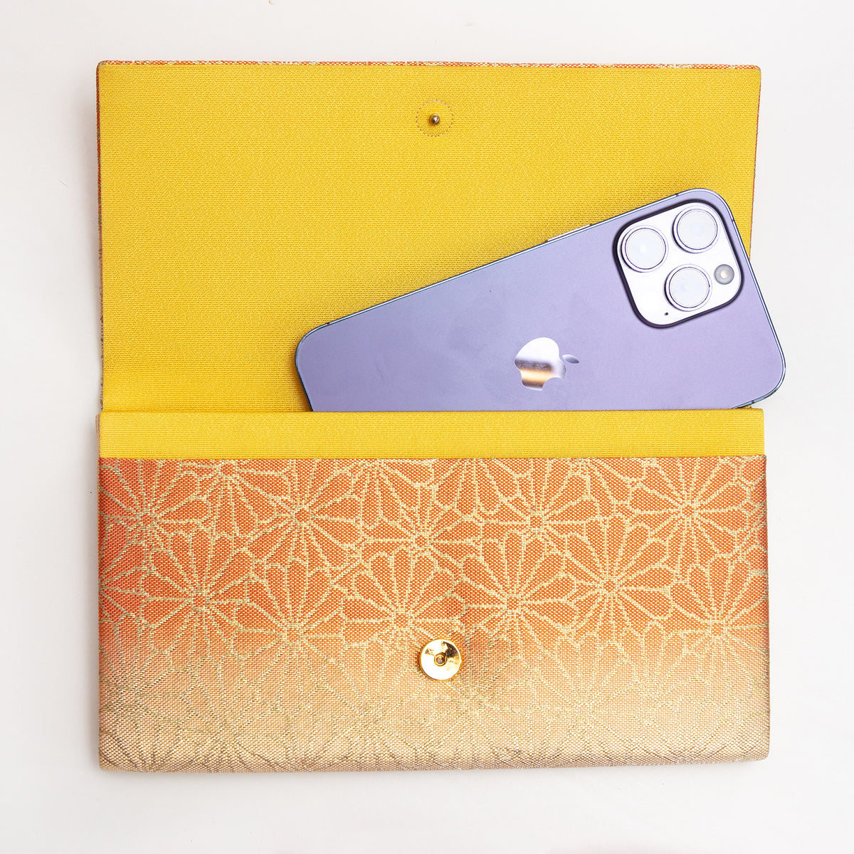 Open gold and orange Japanese silk foldover clutch shown with iPhone 14 Pro Max for scale