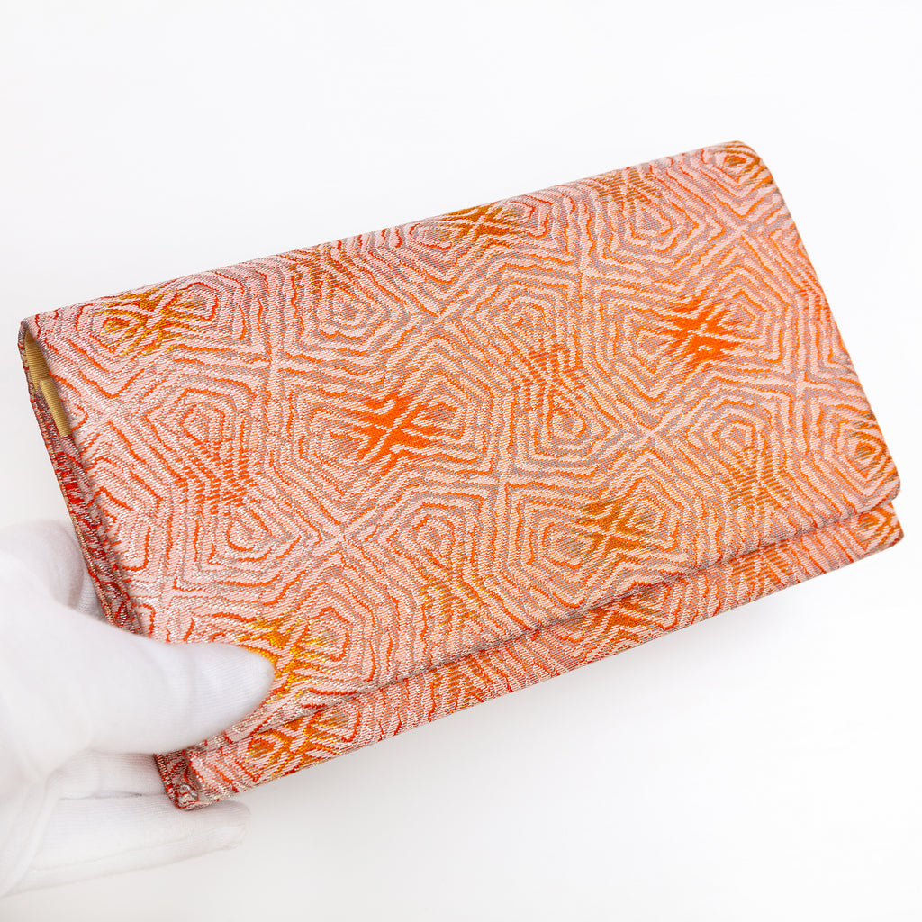 Peach and silver Japanese silk envelope clutch with abstract geometric design, held in a white-gloved hand at a three-quarter angle