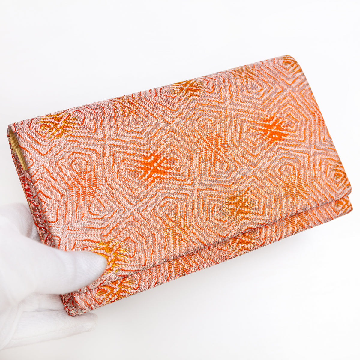 Peach and silver Japanese silk envelope clutch with abstract geometric design, held in a white-gloved hand at a three-quarter angle