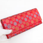 Vermilion red Japanese silk envelope clutch with starburst design, held in a white-gloved hand at a three-quarter angle