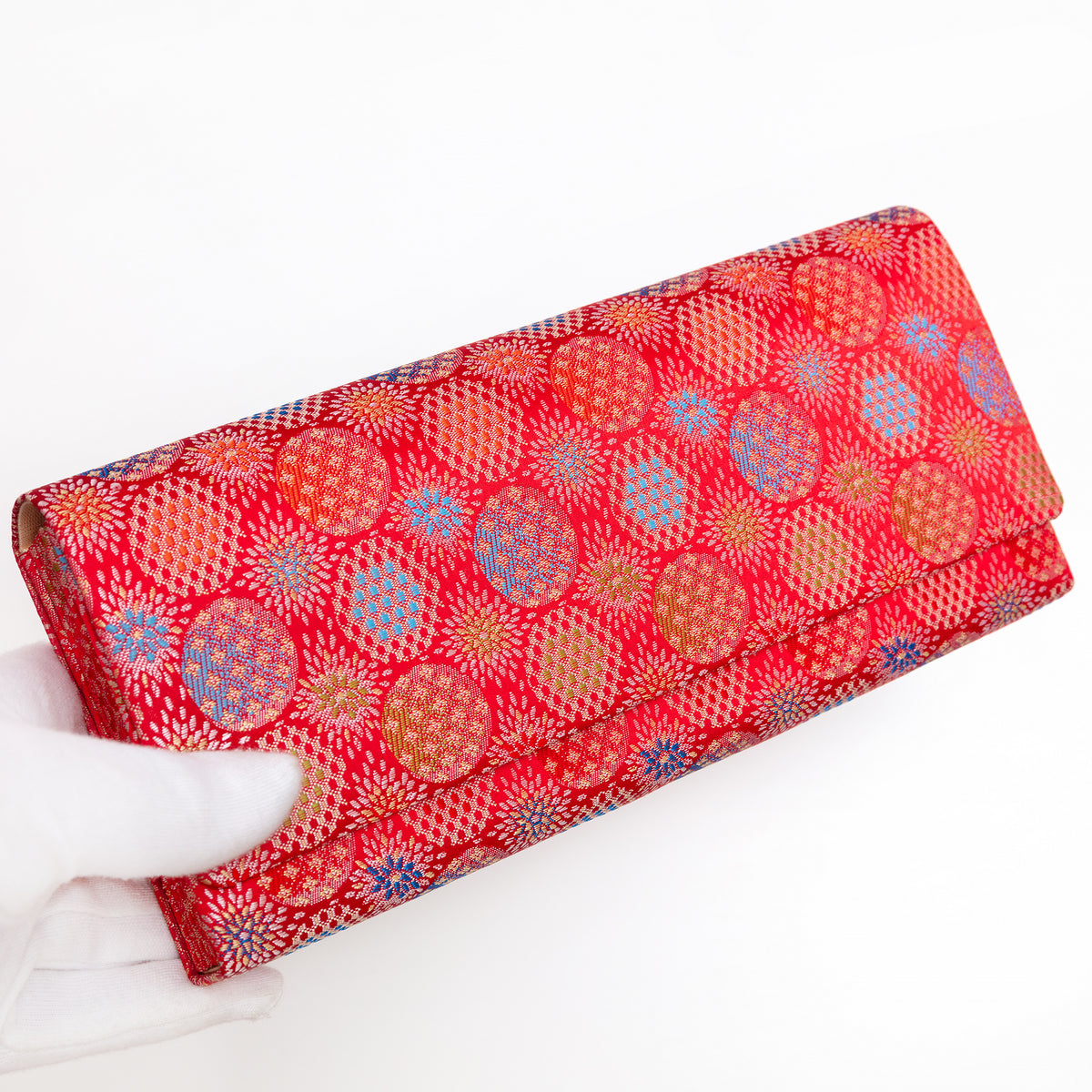 Vermilion red Japanese silk envelope clutch with starburst design, held in a white-gloved hand at a three-quarter angle