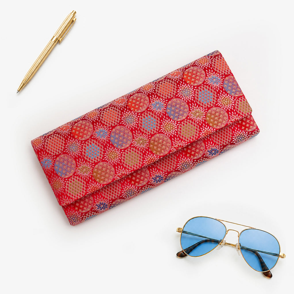 Vermilion red Japanese silk envelope clutch with multicoloured circular starburst design, shown in collector styled flatlay