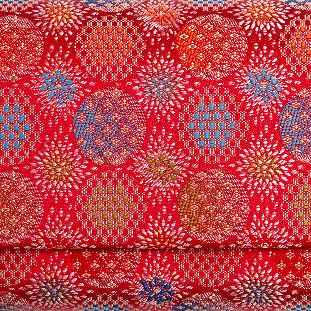 Close-up of finely woven red Japanese silk with peach, olive and blue circular starburst motifs