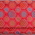 Close-up of finely woven red Japanese silk with peach, olive and blue circular starburst motifs