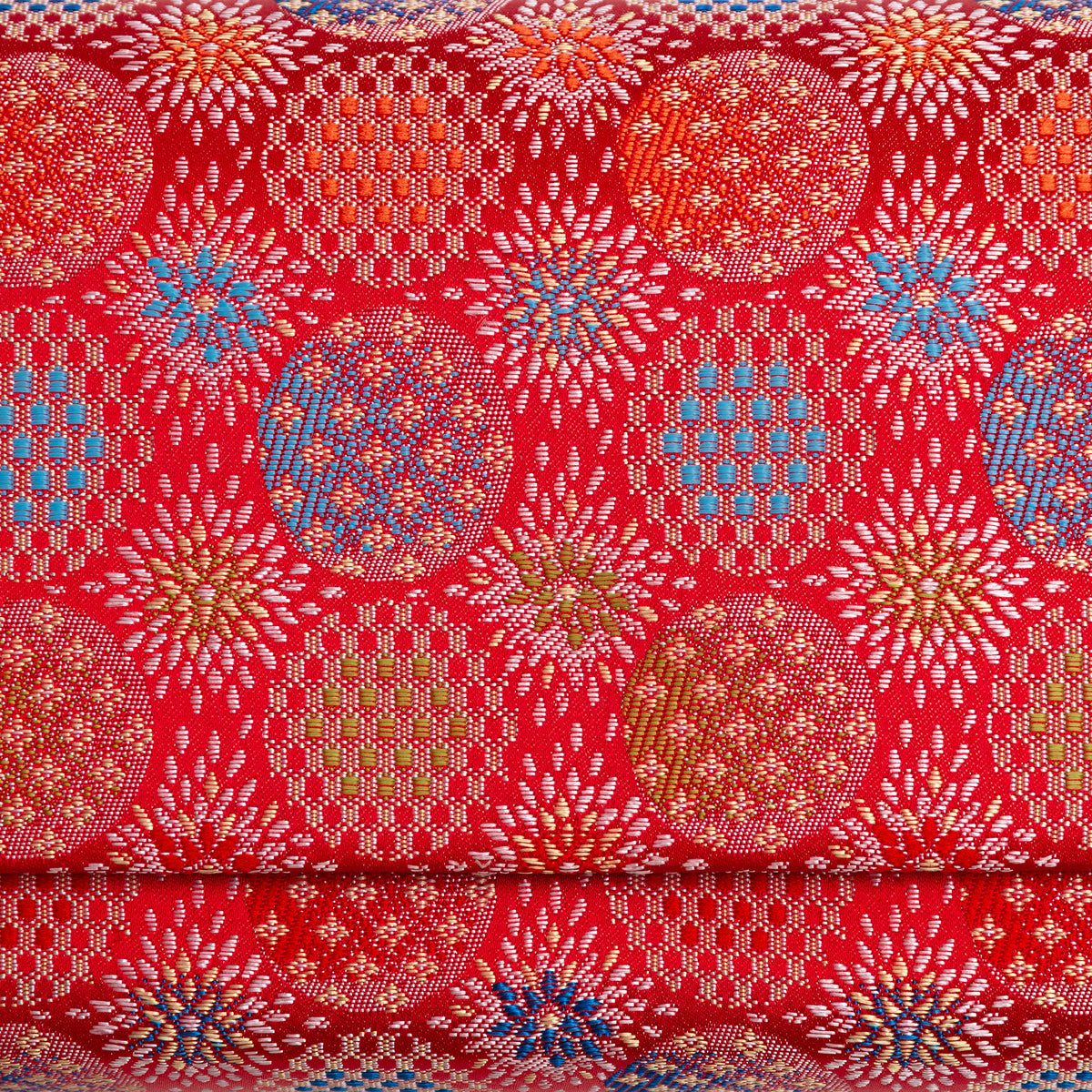 Close-up of finely woven red Japanese silk with peach, olive and blue circular starburst motifs