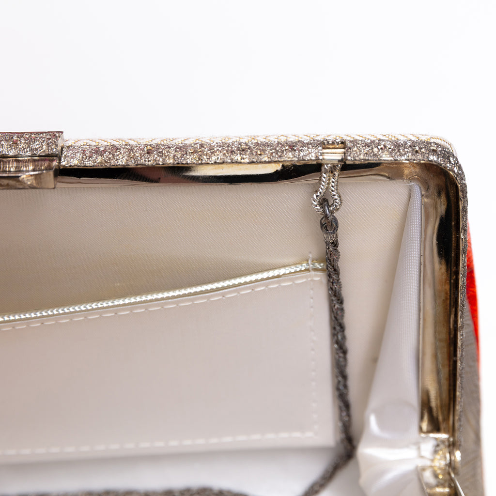 Close-up detail of a clutch handbag frame showing a sparkling silver-tone metal clasp closure, a white interior lining, and a silver trimmed  pocket.