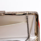 Close-up detail of a clutch handbag frame showing a sparkling silver-tone metal clasp closure, a white interior lining, and a silver trimmed  pocket.