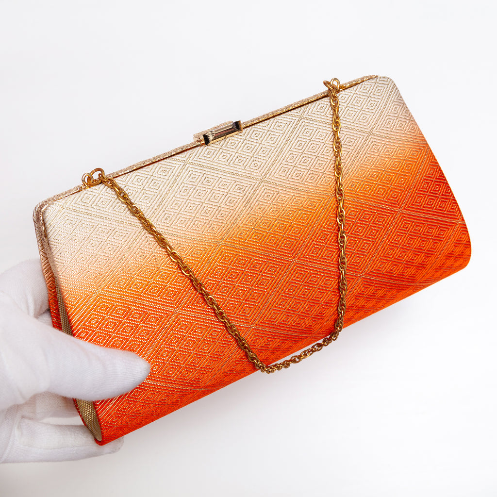 Orange gold kimono silk clutch bag held at three-quarter view with gold-tone chain extended
