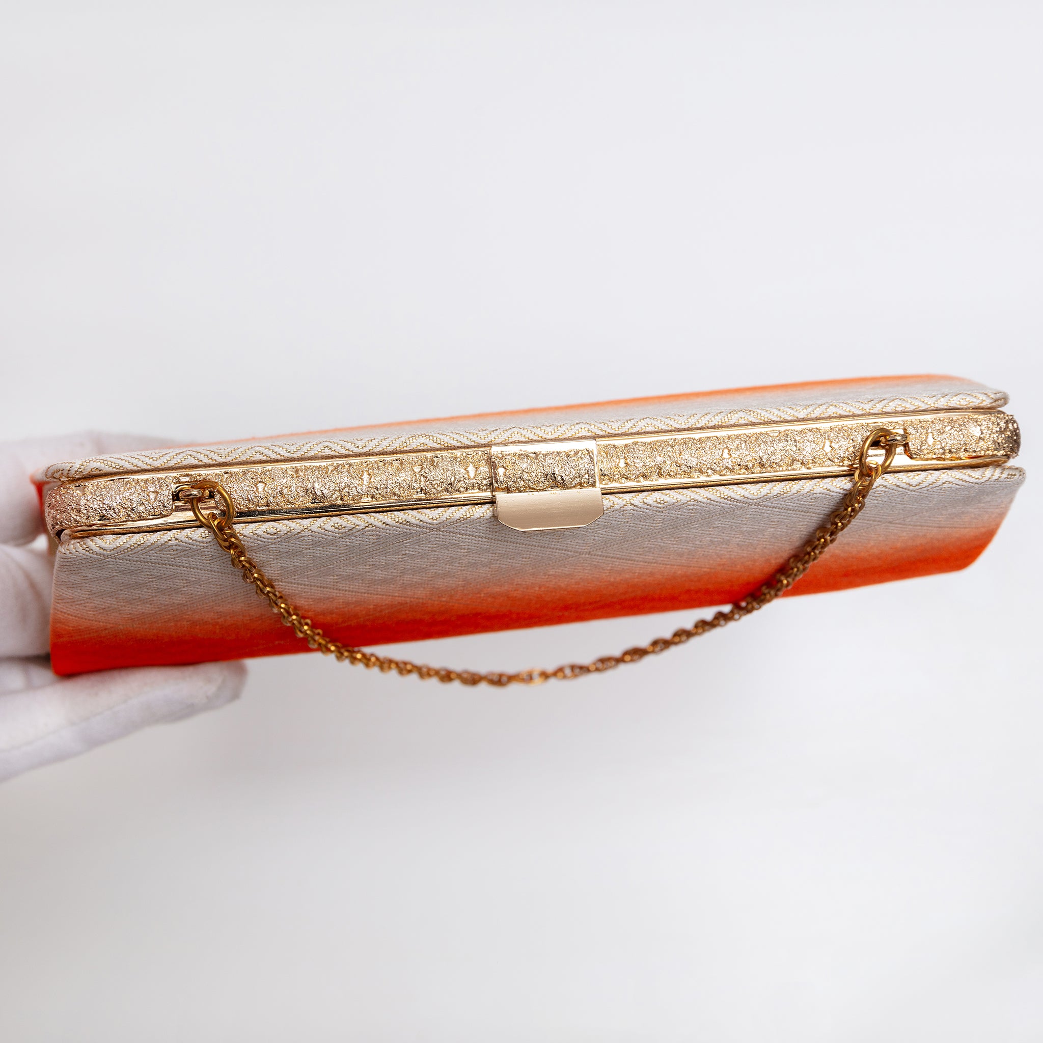 Top view of gold-tone clasp and textured gold-tone frame on vintage Japanese clutch bag. Gold chain strap.