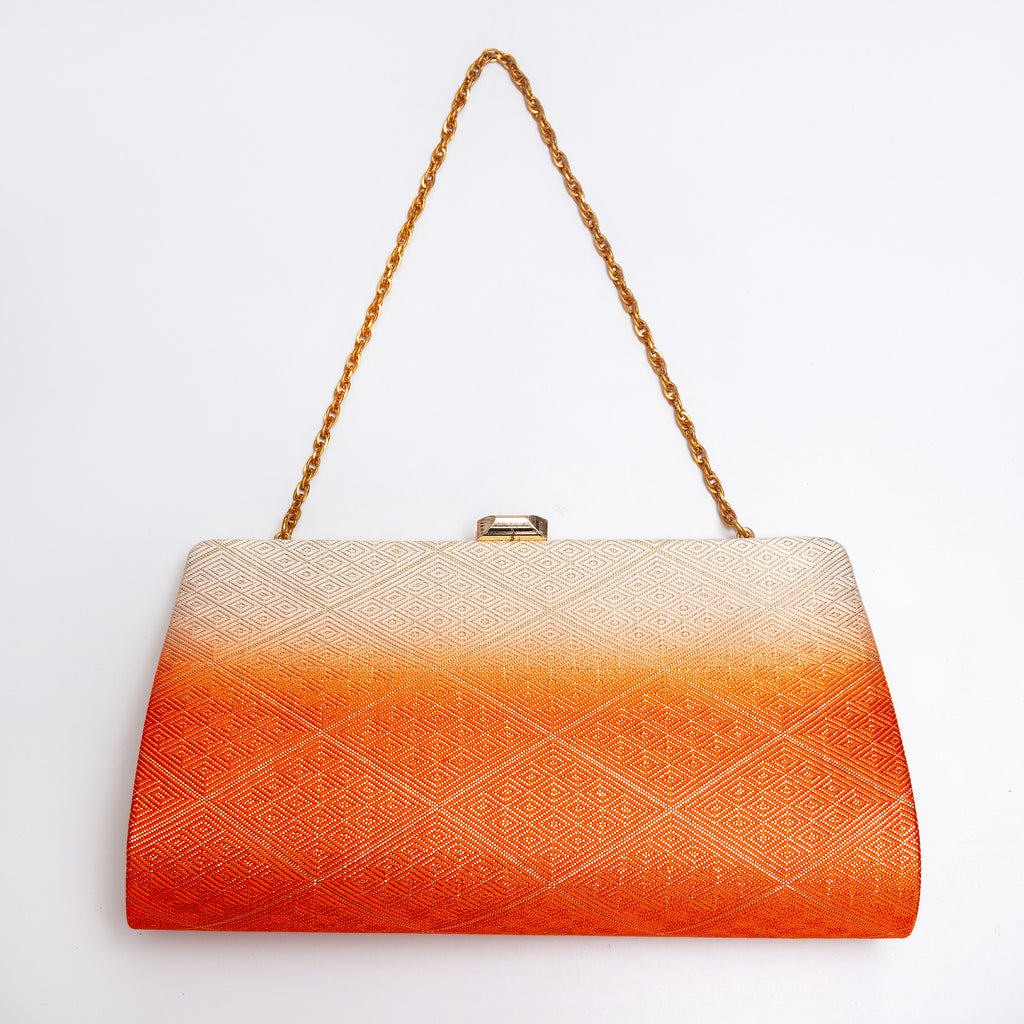 A rectangular vintage Japanese 1970s clutch bag with a gold chain strap and a gold clasp, featuring a textured diamond pattern that fades from cream at the top to bright orange at the bottom, set against a plain white background.