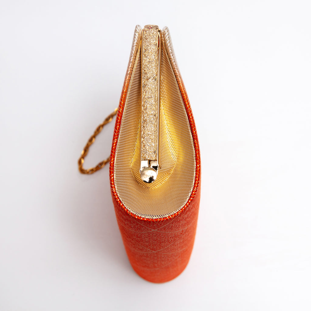 Side view of orange and cream Japanese kimono silk clutch bag with metallic gold silk side panel and textured gold tone bag frame and gold chain strap.