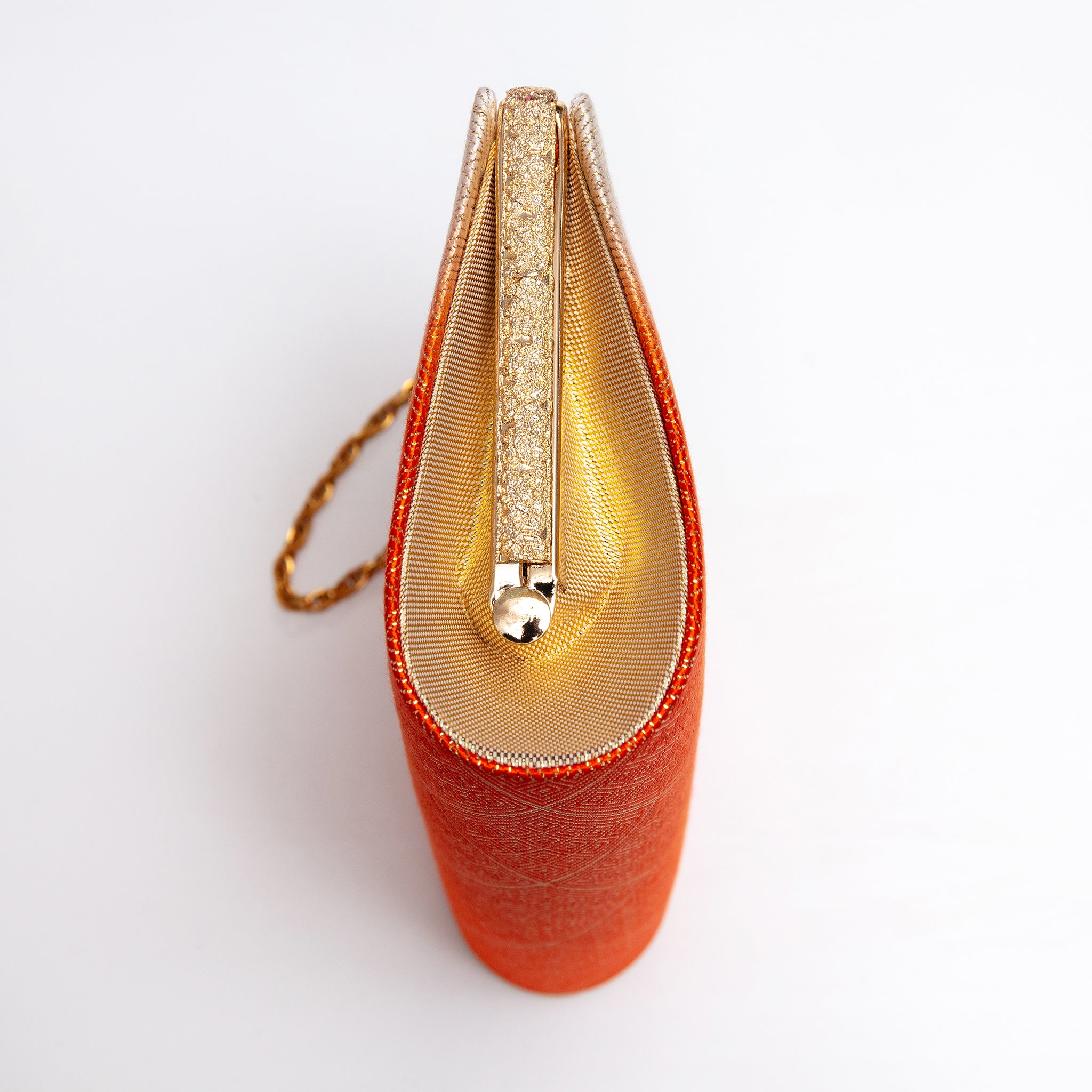 Side view of orange and cream Japanese kimono silk clutch bag with metallic gold silk side panel and textured gold tone bag frame and gold chain strap.