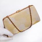 Gold silver kimono silk clutch held at three-quarter view with chunky gold-tone chain extended