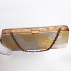 A vintage gold and silver Japanese 1970s silk clutch purse with hexagon geometric pattern, a gold chain strap and decorative textured bag frame and clasp with leaf design.