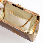 Close-up of the interior of a metallic gold evening clutch bag with a gold chain strap and a cream satin lining, shown on a white background.