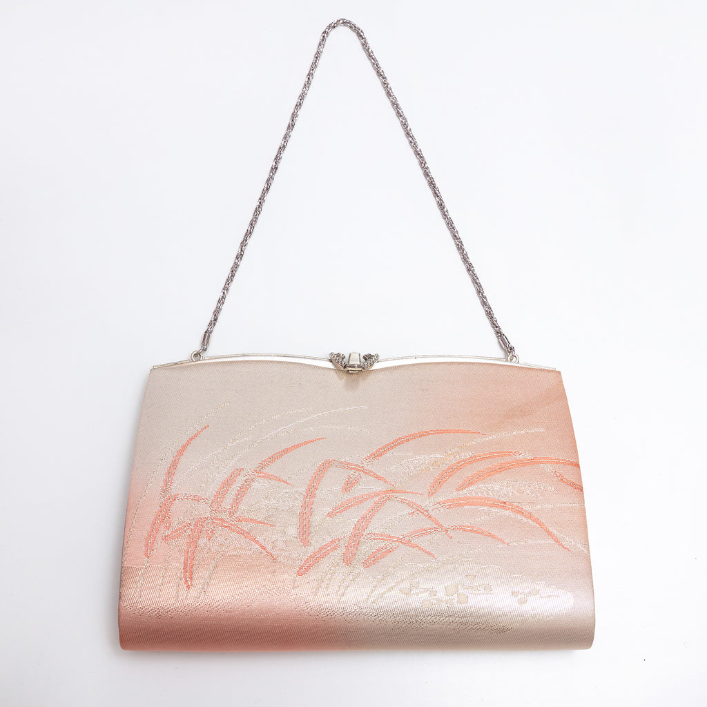 A metallic blush pink clutch purse with a silver chain strap and a silver clasp, decorated with a subtle peach-colored floral pattern on the front. Metallic peach gold and pink Japanese silk clutch bag with windswept grasses