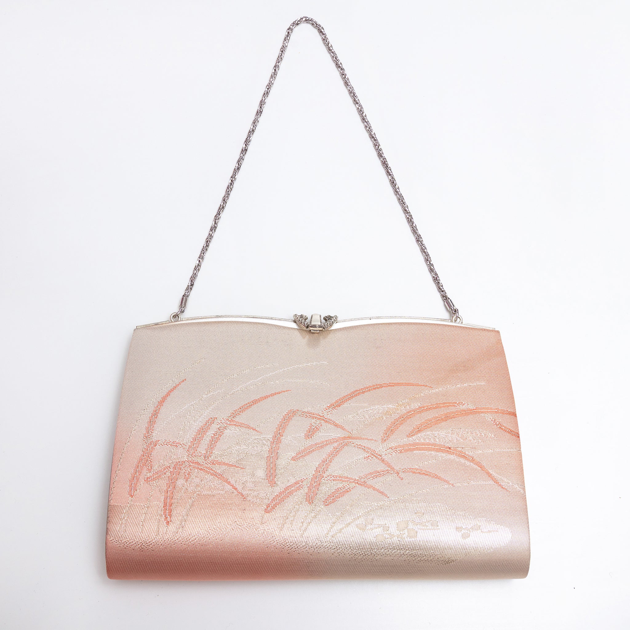 A metallic blush pink clutch purse with a silver chain strap and a silver clasp, decorated with a subtle peach-colored floral pattern on the front. Metallic peach gold and pink Japanese silk clutch bag with windswept grasses