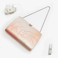 Metallic peach, gold and pink Japanese kimono silk clutch bag with windswept grass design and ornate Cupid’s-bow frame, shown in styled flatlay. Silver chain strap.