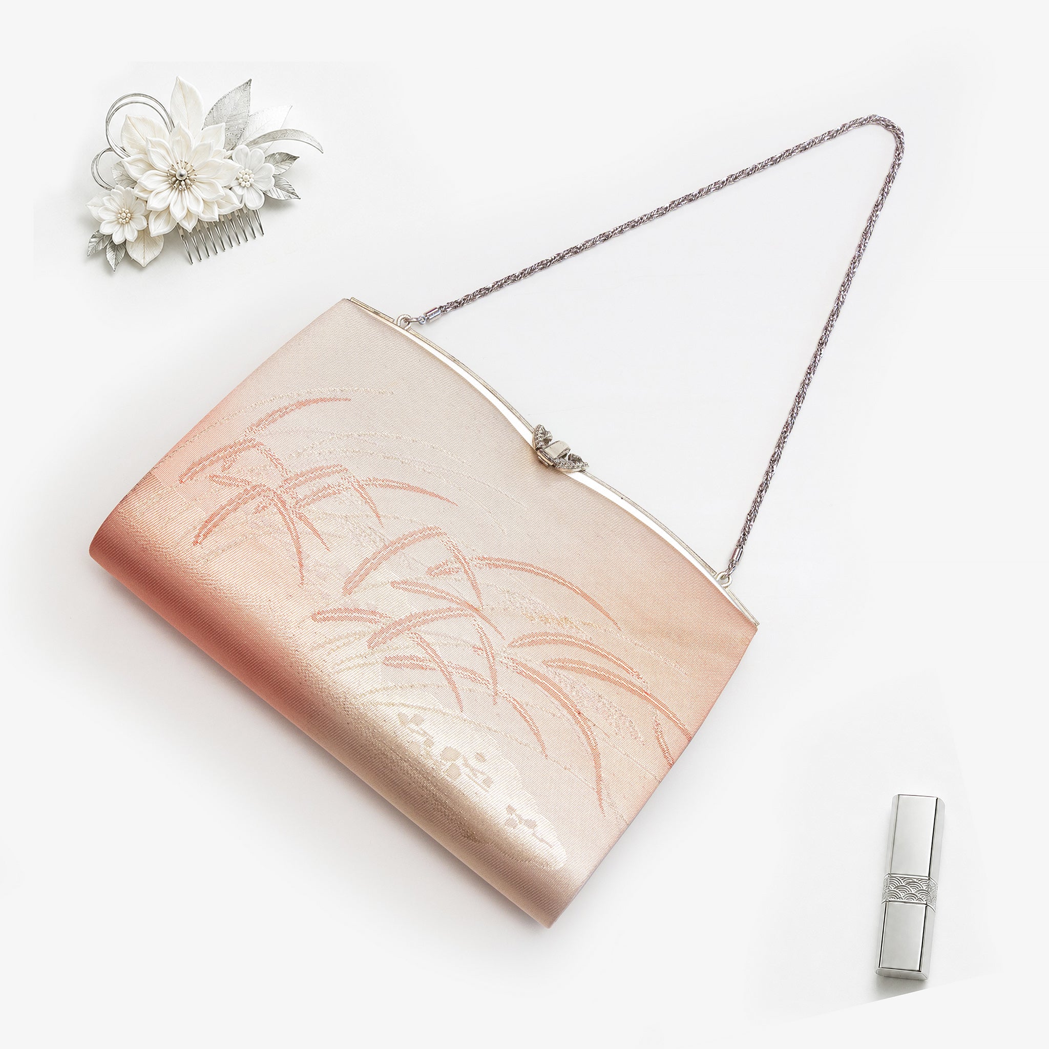 Metallic peach, gold and pink Japanese kimono silk clutch bag with windswept grass design and ornate Cupid’s-bow frame, shown in styled flatlay. Silver chain strap.