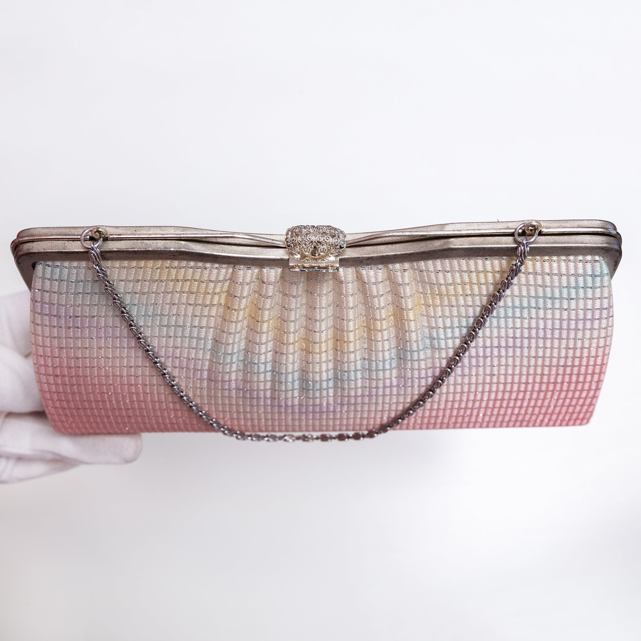 A vintage 1970s Japanese silk evening clutch purse with a pleated, grid-textured body in a pastel rainbow gradient, featuring a silver-tone metal frame, rhinestone-embellished clasp, and a silver chain strap. The clutch is held by a white gloved hand against a plain white background.