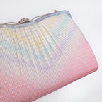 A close-up of a textured 1970s Japanese kimono silk evening clutch bag with a pastel rainbow gradient transitioning from light blue and yellow at the top to soft pink at the bottom, featuring a silver-tone metal frame and clasp.