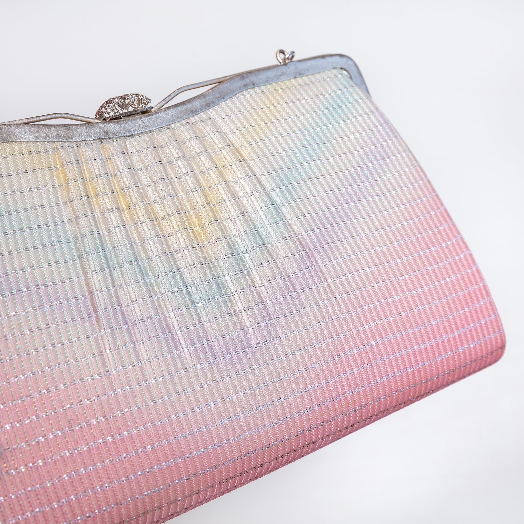 A close-up of a textured 1970s Japanese kimono silk evening clutch bag with a pastel rainbow gradient transitioning from light blue and yellow at the top to soft pink at the bottom, featuring a silver-tone metal frame and clasp.