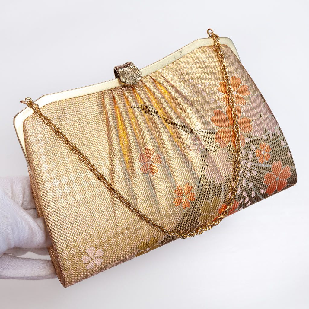 Gold crane kimono silk clutch held at three-quarter view with gold-tone chain extended and fancy gold clasp.