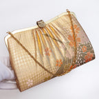 Gold crane kimono silk clutch held at three-quarter view with gold-tone chain extended and fancy gold clasp.