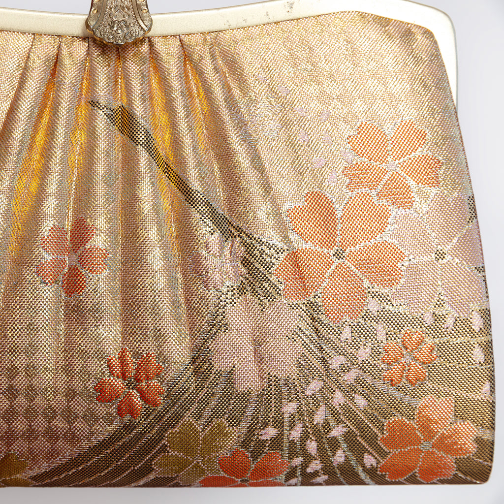 A close-up of a vintage metallic gold Japanese silk clutch purse featuring a stylised crane and cherry blossom pattern in orange, peach, and gold tones.