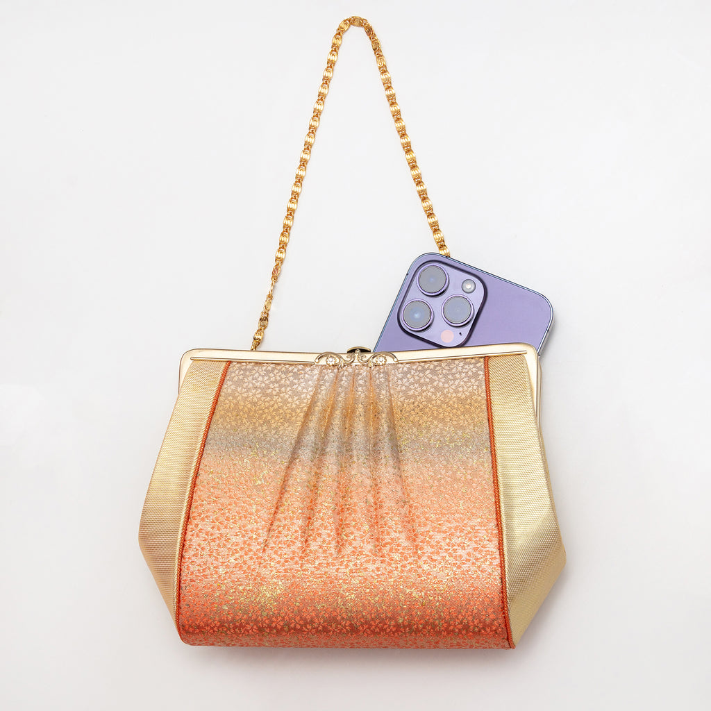 Sculptural orange and gold Japanese silk clutch bag shown with iPhone 14 Pro Max for scale