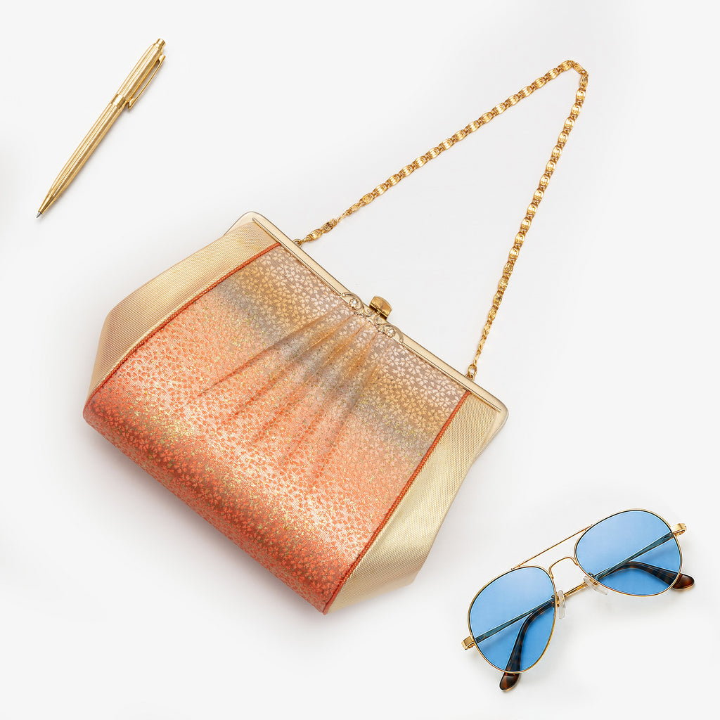 Burnt orange, blue-grey and gold metallic Japanese silk clutch bag with abstract ombré design and sculptural shape, shown in styled flatlay