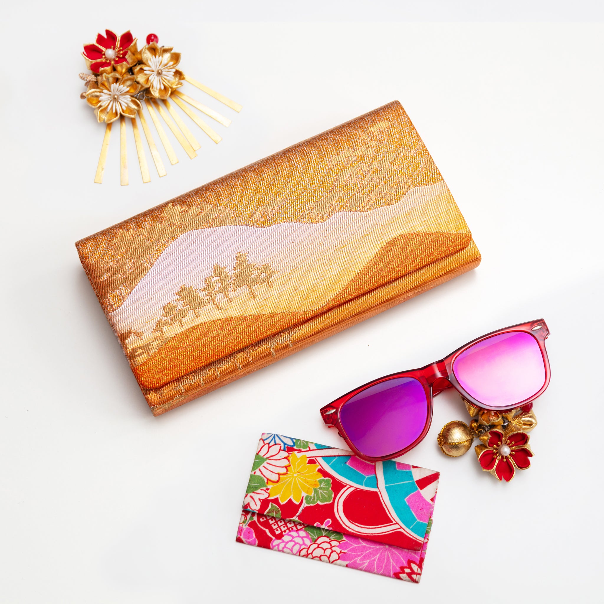Metallic gold and bronze vintage clutch bag with landscape scene on a white background surrounded by accessories.
