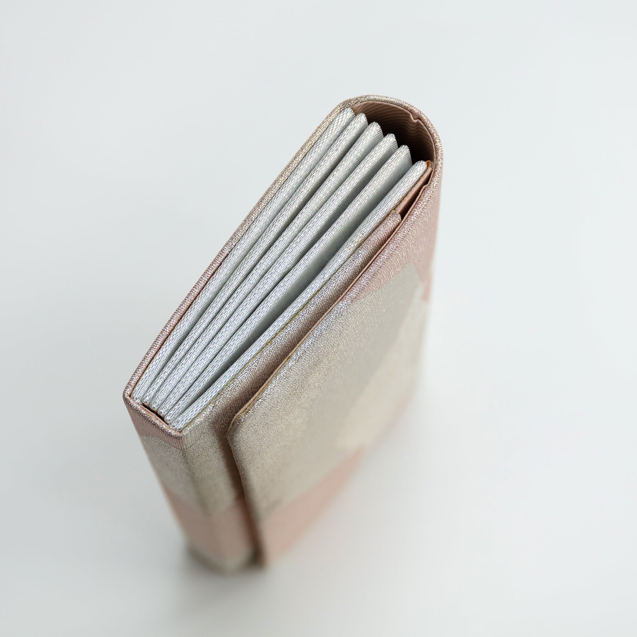 Side view of a vintage Japanese silk fold over clutch bag with silver concertina edge. On white.