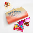 Peach and yellow vintage Japanese silk clutch bag with peacock and fan design on a white surface surrounded by accessories and sunglasses.