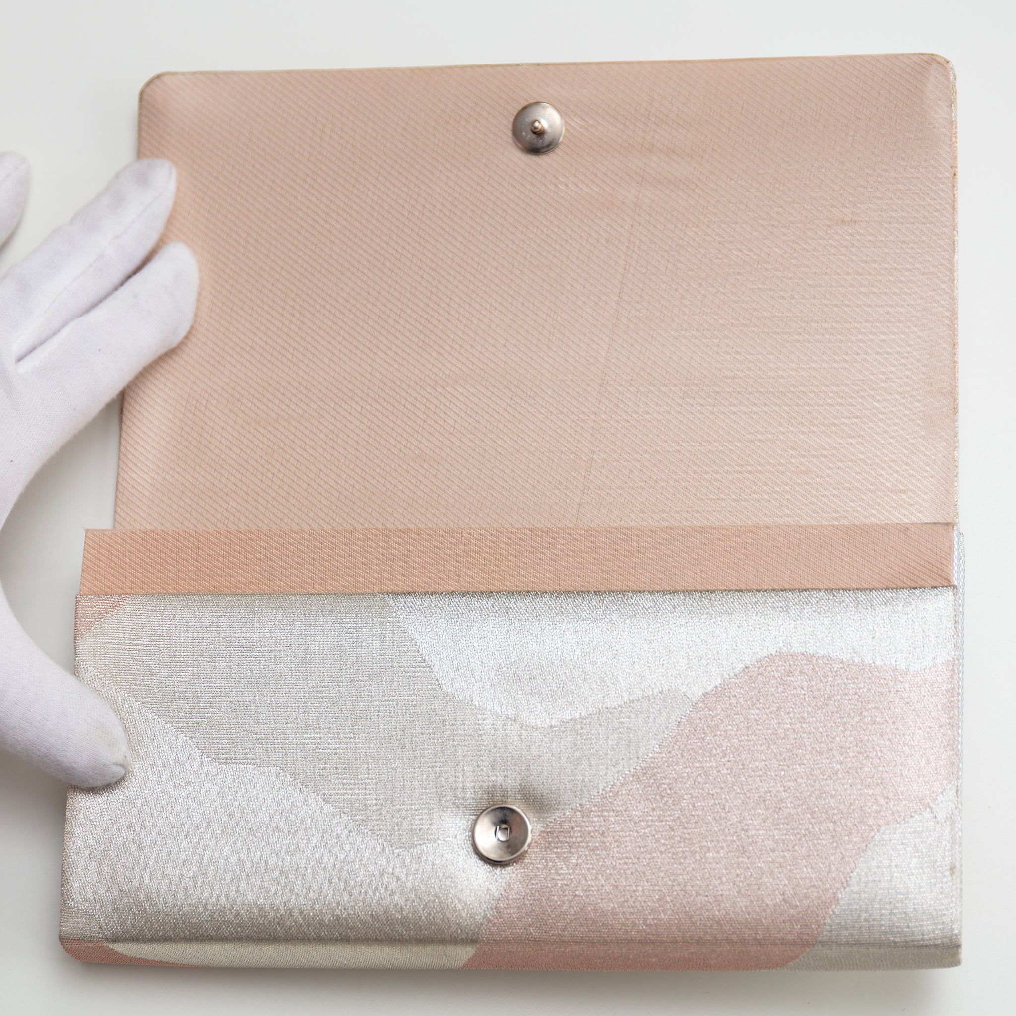 Vintage Japanese silk clutch bag held open by gloved hand showing the pale pink silk twill lining and silver metal closure stud.