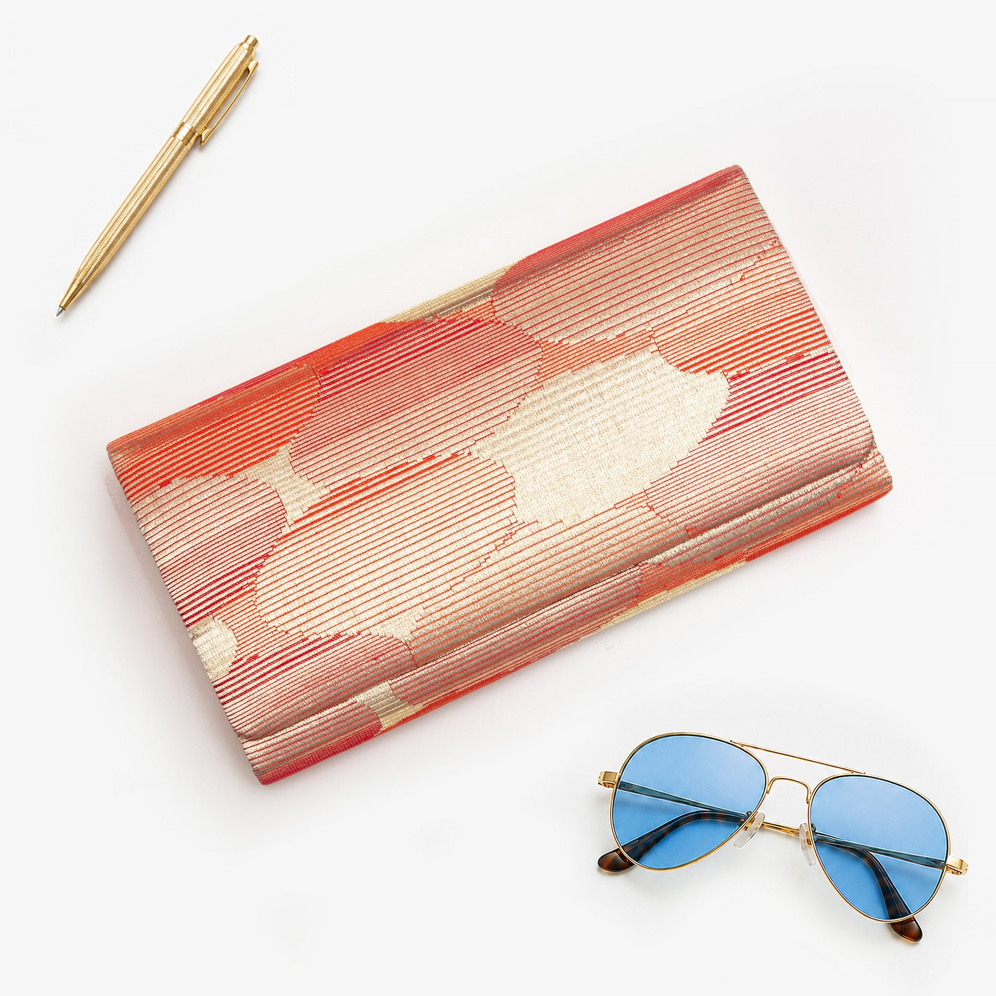 Red-gold vintage Japanese silk clutch bag, abstract cloud pattern, styled with sunglasses and gold pen
