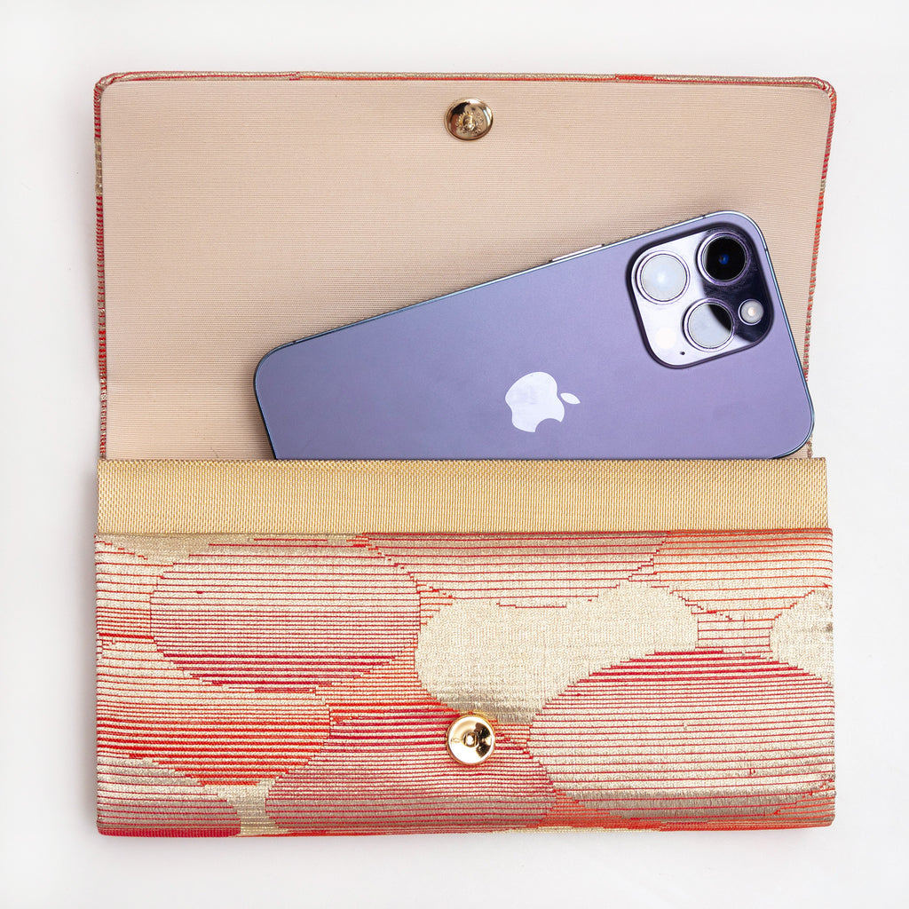 Red-gold kimono silk clutch bag shown with iPhone 14 Pro Max for scale