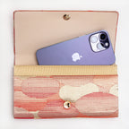 Red-gold kimono silk clutch bag shown with iPhone 14 Pro Max for scale